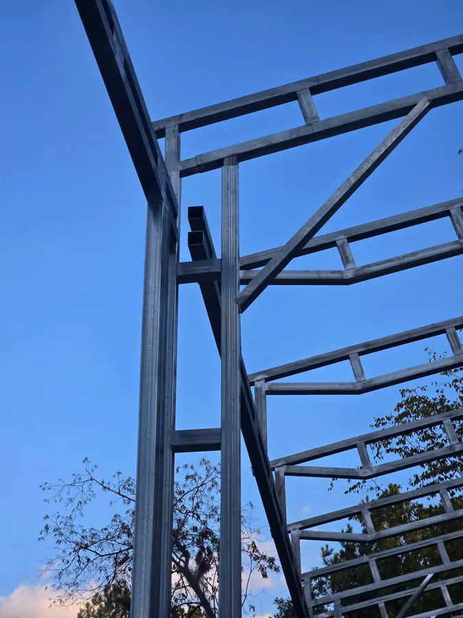Corner of the steel frame seen from below, showing the column, header, a diagonal brace and two open tube ends