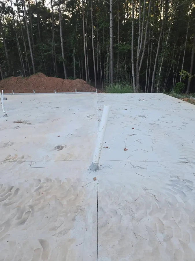 A white PVC plumbing stub-up leaning sharply to one side in the slab, with tire tread marks on the concrete