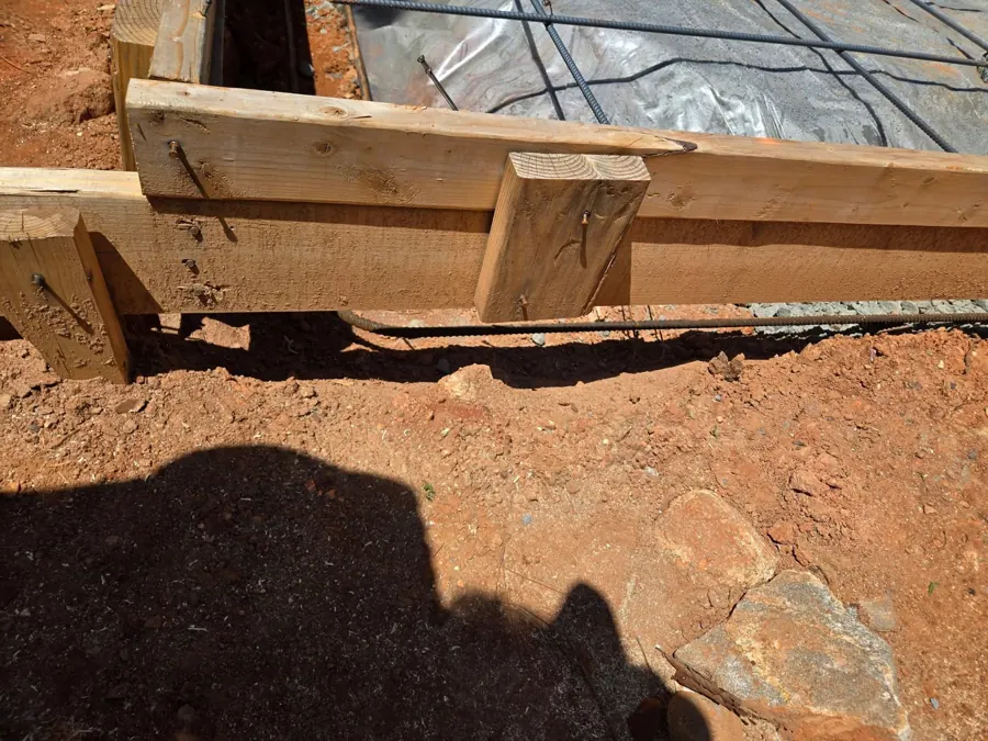 Wooden form boards at the edge of the slab before the pour, with rebar, vapor barrier and a footing trench visible